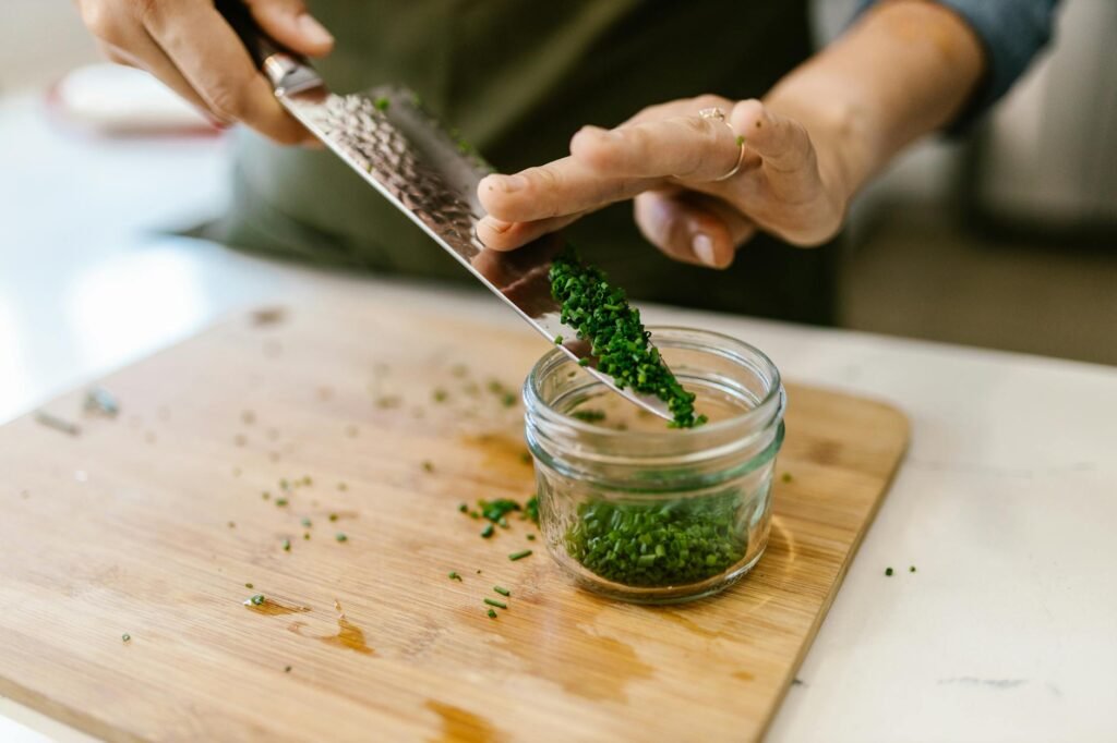 Hands trimming fresh chives and parsley over a cutting board during meal prep