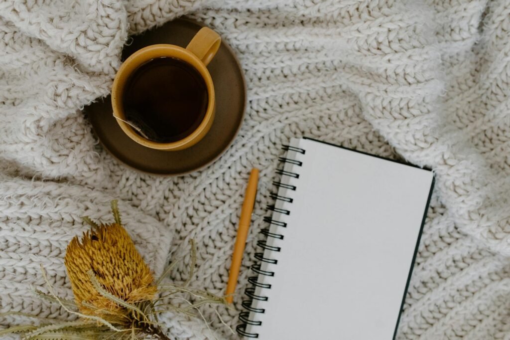 A small mug of herbal tea beside a notebook and pen on a tidy nightstand