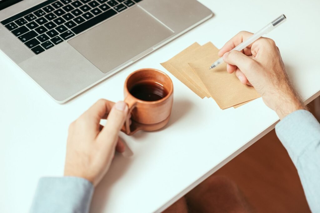 A laptop and handwritten comparison notes laid out beside a mug and supplement containers.